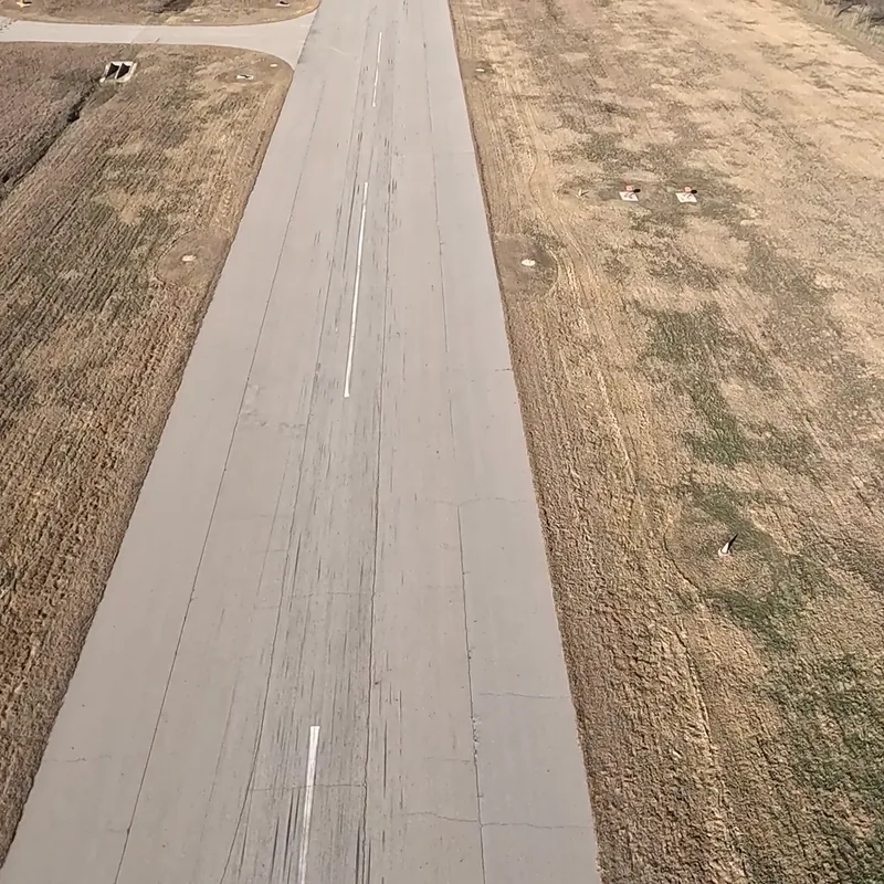 Aerial view down a runway centerline, with the shadow of a small airplane on the grass alongside